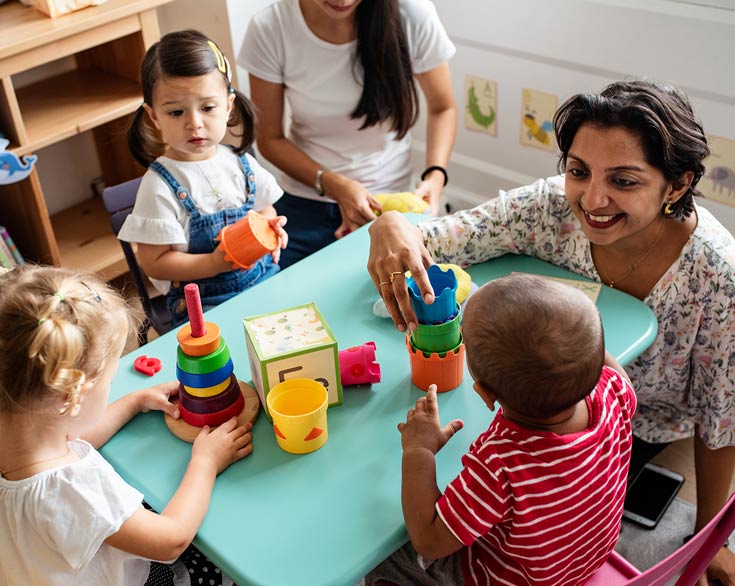 Photo of small children playing in day care with happy teacher