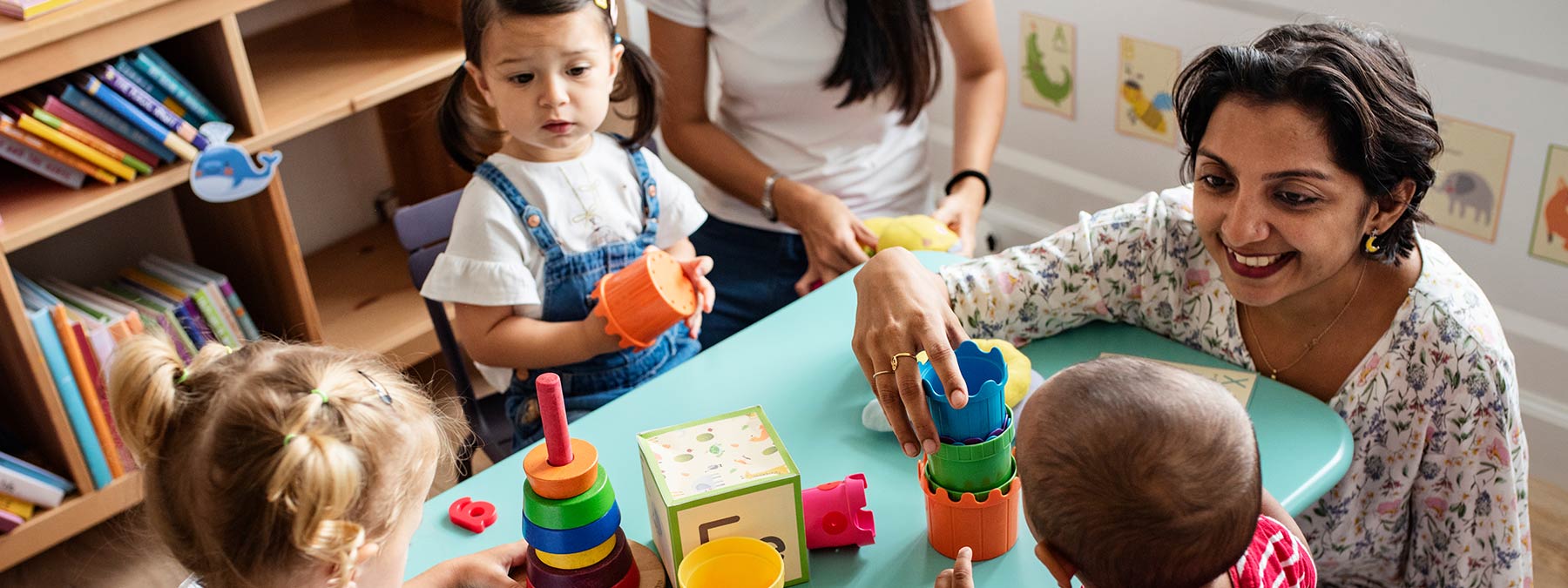 Photo of small children playing in day care with happy teacher