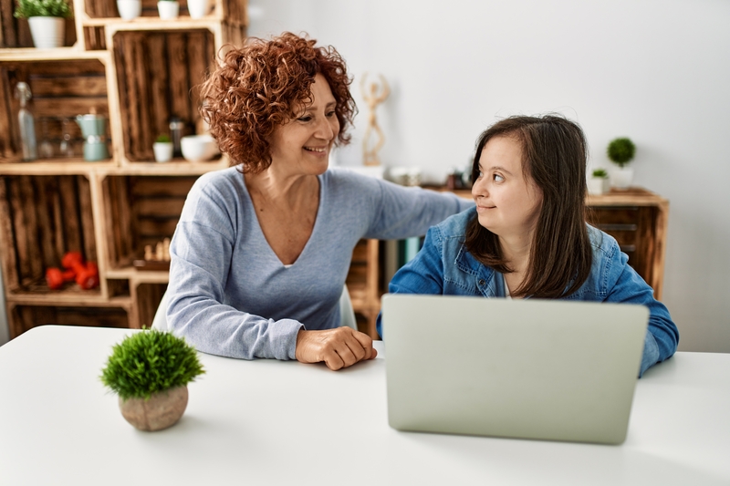 Mature woman and down syndrome young female adult having a discussion at a computer